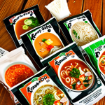 **

A close-up shot of various instant soup packets, some recognizable brands and some with Asian-inspired labels (Ramen, Pho), arranged on a wooden table. Focus on the ingredient lists and nutritional information panels. Include some fresh vegetables (carrots, green onions) and spices (chili flakes) scattered around, suggesting ways to personalize the soup. Lighting should be bright and inviting.

**